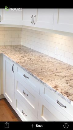 a kitchen with white cabinets and marble counter tops