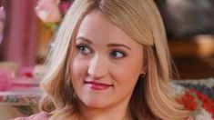 a woman with blonde hair sitting in a chair and looking at the camera while wearing a pink top