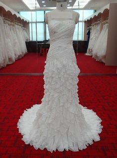 a white wedding dress is on display in a room with red carpet and large windows