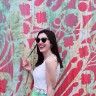 a woman wearing sunglasses standing in front of a wall covered with red and green flowers