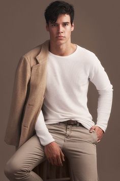 a man sitting on top of a wooden chair wearing a white shirt and tan pants