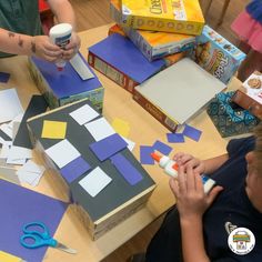 two children sitting at a table with construction paper and scissors