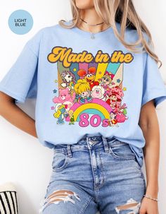 Step into a time machine of memories with our "Born in the 80s Nostalgia Retro Blast Tee." This vintage-inspired shirt is a vibrant tribute to the iconic era, featuring beloved characters like Strawberry Shortcake and her whimsical friends. Crafted from soft, comfortable fabric, this tee not only celebrates the spirit of the 80s but also offers a cozy fit for everyday wear. The lively design showcases a medley of colorful characters, bringing a burst of nostalgia to your wardrobe. Whether you're reliving your own 80s adventures or introducing the magic to a new generation, this tee is a perfect way to make a statement. Embrace the charm, fun, and enduring appeal of the 80s with every step you take in this delightful piece. Join us in celebrating the era that left an indelible mark on pop c Retro Blue T-shirt With Cartoon Print, Retro Character Print T-shirt For Fan Conventions, Vintage Crew Neck T-shirt With Cartoon Print, Vintage Crew Neck T-shirt With Character Print, Vintage Cotton T-shirt With Cartoon Print, Retro T-shirt With Screen Print For Fan Conventions, Retro Graphic Print T-shirt For Fan Conventions, Vintage Cartoon Print Fan Merchandise T-shirt, Retro Crew Neck T-shirt With Character Print