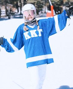 a woman in a blue and white hockey uniform holding her arms out while standing on skis