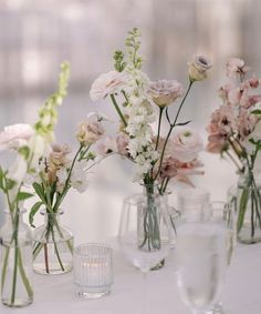 several vases filled with different types of flowers on a white tablecloth covered table