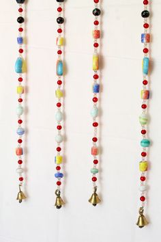 three necklaces with bells hanging from them on a white wall next to each other