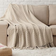 a couch with a blanket on top of it next to a pillow and rug in front of a brick wall