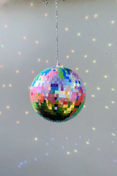 a multicolored disco ball hanging from a chain in front of a white wall