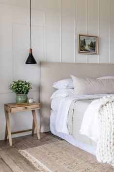 a bed with white linens and pillows in a bedroom next to a wooden table