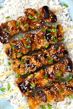 chicken skewers with sesame seeds and rice on a blue plate