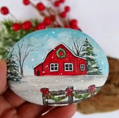 a painted rock with a red barn and wreath on it