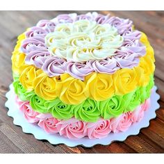 a multicolored cake on a white plate sitting on a wooden table with flowers