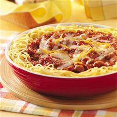 a red bowl filled with spaghetti and sauce on top of a wooden table next to a plate of bread