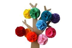 colorful felt flowers are hanging from a tree with clothes pins attached to the top of them