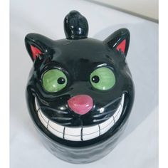 a black ceramic cat with green eyes and fangs on it's face is shown