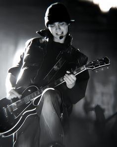 a man with a guitar in his hand and wearing a hat, black leather jacket and boots