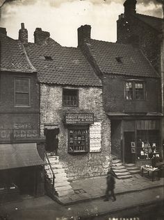 an old black and white photo of a man walking down the street in front of some buildings