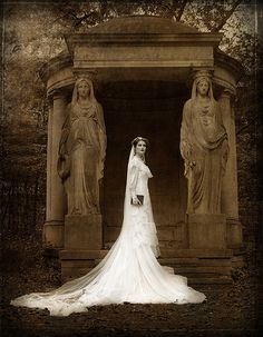 a woman standing in front of statues wearing a wedding dress with veil on her head