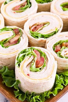 several wraps with bacon and lettuce are on a wooden platter, ready to be eaten