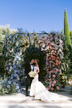 a bride and groom standing in front of a flower wall