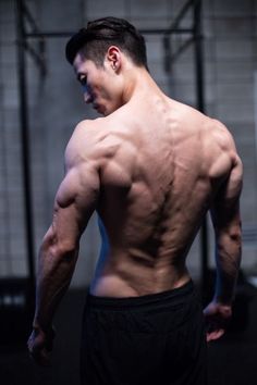 a man with no shirt on standing in a gym looking down at his chest and back