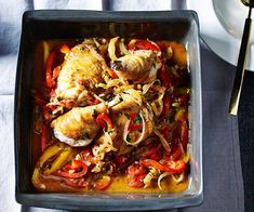 a pan filled with chicken and peppers on top of a table next to a white plate