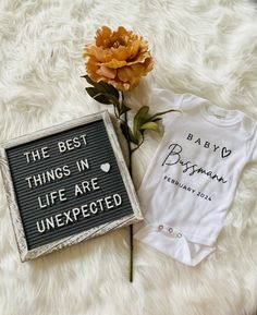 a baby's t - shirt next to a sign that says the best things in life are unexpected