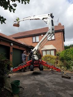 two men are working on a large crane in front of a brick house with green doors