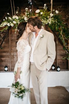 a bride and groom kissing in front of an arch with greenery on the wall