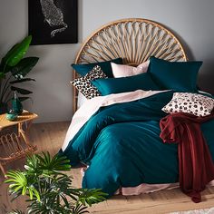 a bed with green comforter and pillows in a room next to a plant on the floor