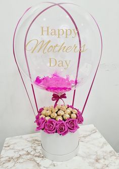 a vase filled with flowers and chocolates on top of a marble table next to a sign that says happy mother's day