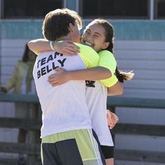 two young people hugging each other in front of a soccer field with the words team belly written on it