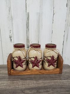 three ceramic jars with red stars on them are sitting in a wooden tray against a white wall