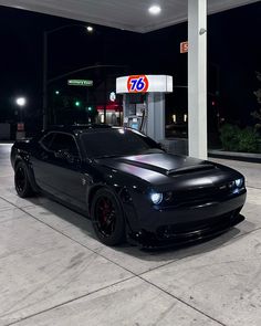 a black sports car parked in front of a gas station at night with the lights on