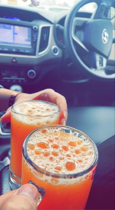 two people are holding orange drinks in their hands while driving the car with steering wheel behind them