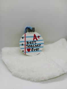 a badge with the words, best teacher ever on it sitting on a white blanket