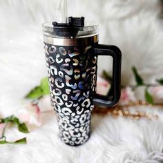 a black and white leopard print travel mug with a gold chain on the side, next to flowers