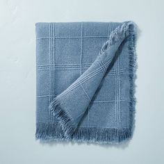 a light blue blanket with fringes on it sitting on top of a white wall