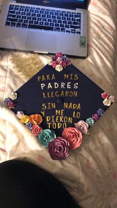 a laptop computer sitting on top of a bed next to a graduation cap with flowers