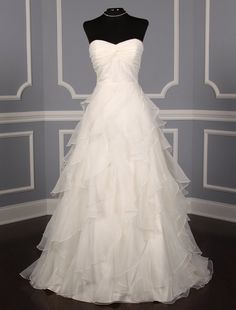 a wedding dress on display in front of a gray wall with white trimmings