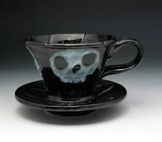 a black and white cup with a skull in the middle sitting on a saucer