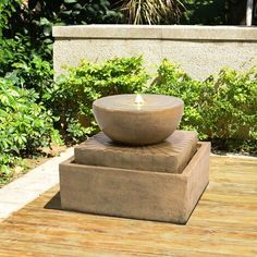 an outdoor fountain on a wooden deck in front of some bushes and shrubbery,