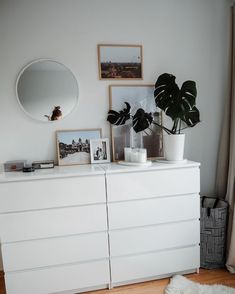 a white dresser with some pictures on it and a potted plant next to it