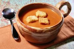 a bowl filled with soup and croutons on top of a napkin next to a spoon