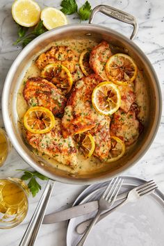 a pan filled with chicken and lemons on top of a table next to silverware