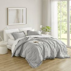 a bedroom with white walls and wood flooring has a large bed covered in grey linens