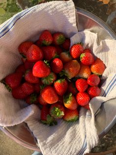 a metal bowl filled with lots of strawberries on top of a table next to a white towel