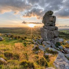 the sun is setting behind some rocks on top of a grassy hill with grass and bushes