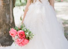 a woman in a white wedding dress holding a bouquet of pink flowers and greenery