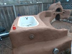 an outdoor bathtub made out of clay in the back yard with a sink and fire hydrant